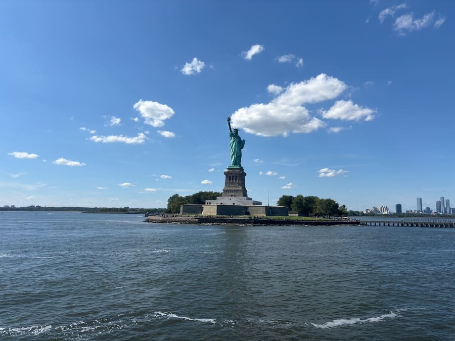 Statue of Liberty across New York Harbor beneath a bright blue sky