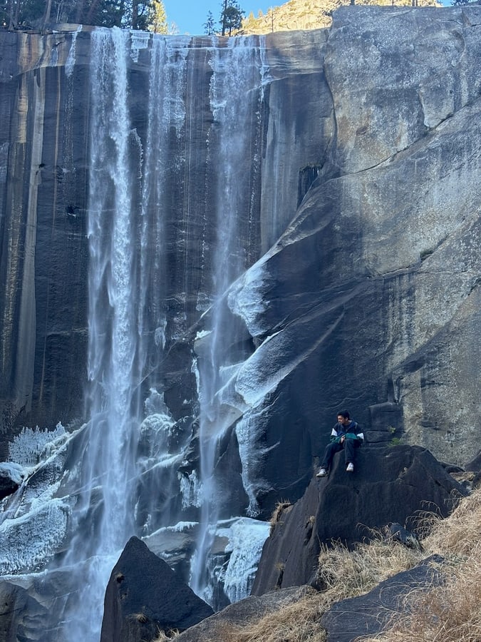 Hiker standing beneath a frozen Yosemite waterfall