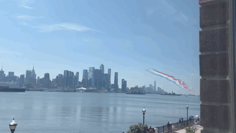 Aircraft trailing red, white, and blue smoke above the Manhattan skyline across the Hudson River